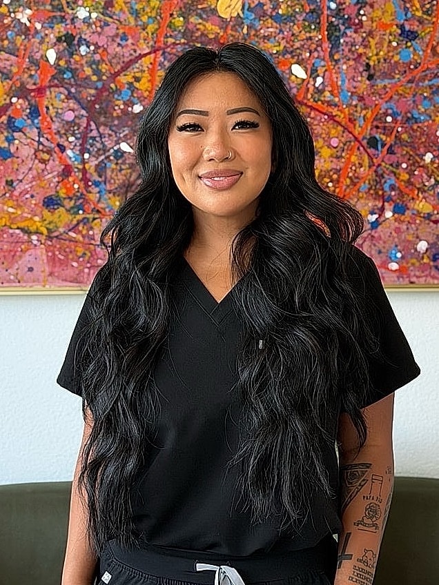 Person in black scrubs smiling by colorful artwork.