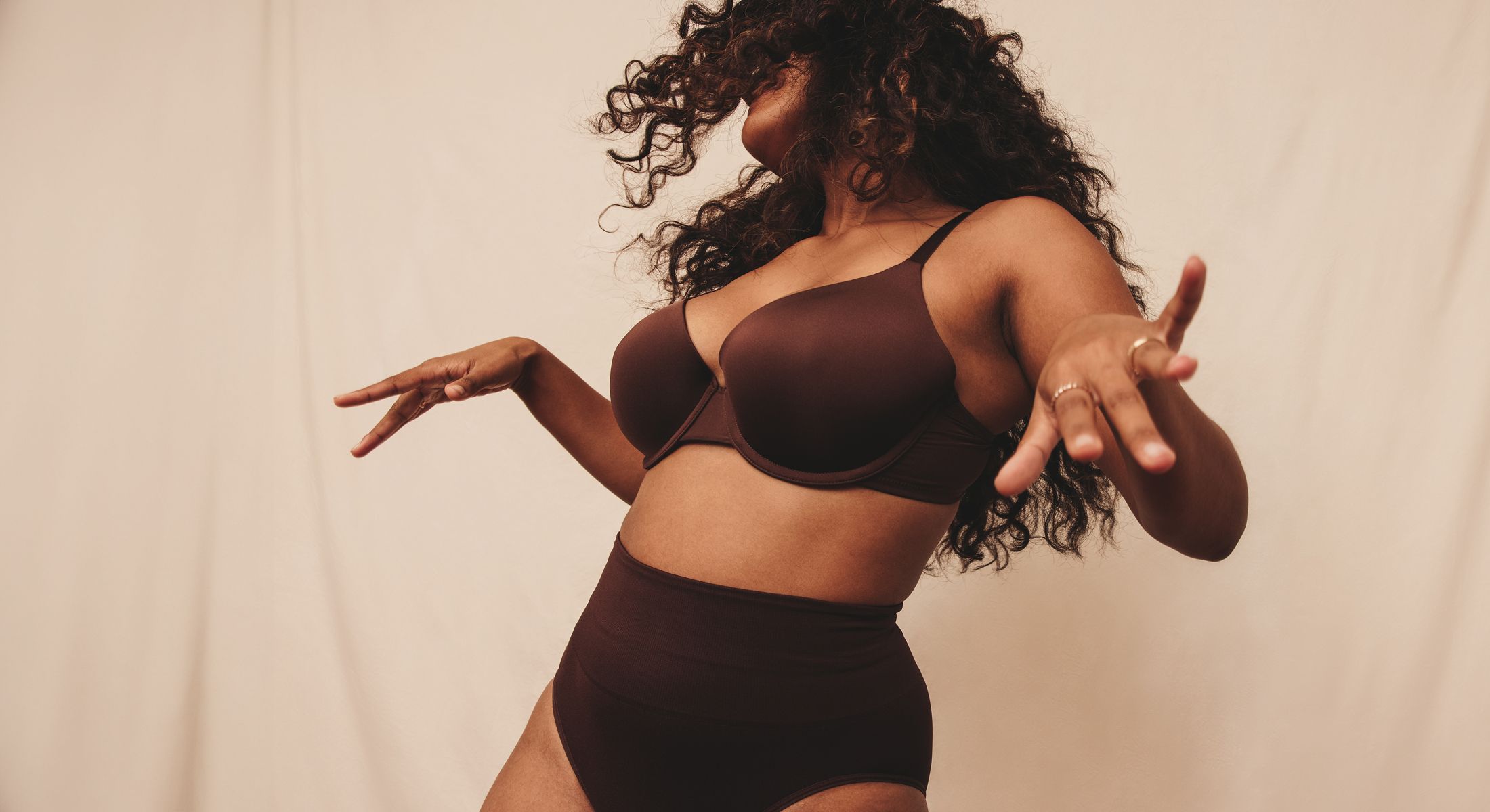 Person dancing, wearing dark lingerie against backdrop.